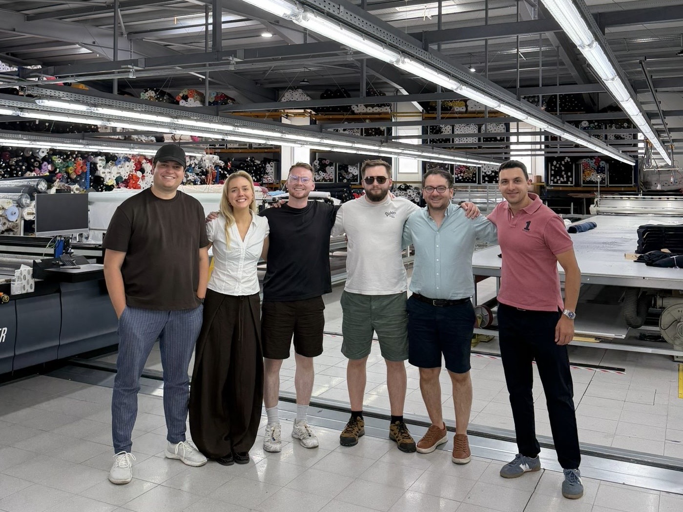 The Ameba team standing together in a textile warehouse surrounded by rolls of fabric.
